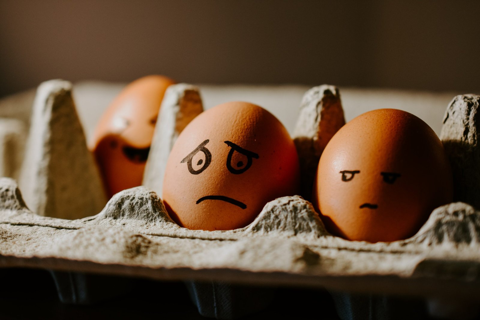 two brown, hard-boiled eggs in a cardboard carton, with sad faces drawn on them