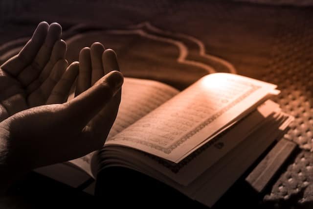 Photo: A pair of hands are cupped over a copy of the Koran. The light is dim, but a shaft of sunlight shines on the book.