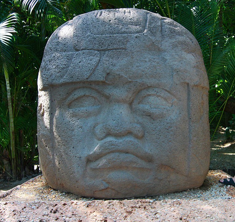 A large, round head carved from stone. The face has rounded features, and is roughly as tall as it is wide. The colossal Olmec heads are one piece of material culture from Mesoamerican that have been claimed by Book of Mormon theorists who believe some of the the Book's events took place in ancient Mesoamerica.