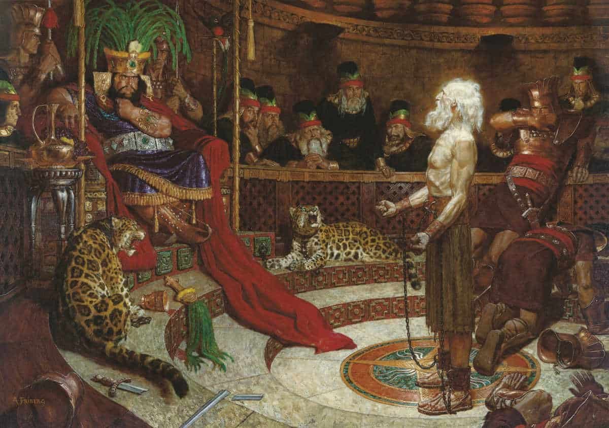 An image of Arnold Friberg’s painting, "Abinadi before King Noah," in which a chained White man with a long white beard stands before a brown-skinned king king wearing lush fabrics and seated on a gold throne. The painting depicts a scene described in the Book of Mormon. Maya motifs, like the green feathers of the quetzal bird, are sprinkled throughout. 